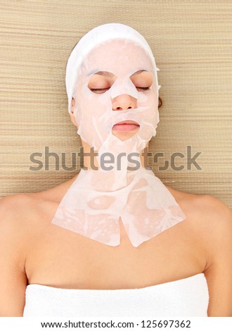Young woman with cloth facial mask, on bamboo mat background