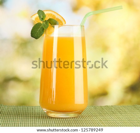 Glass of orange juice with mint on table on bright background