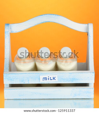 Milk in bottles in wooden box on orange background