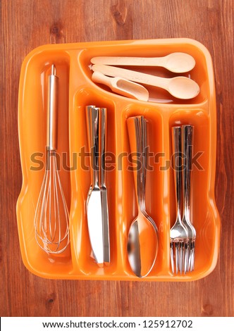 Orange plastic cutlery tray with checked cutlery and wooden spoons on wooden table