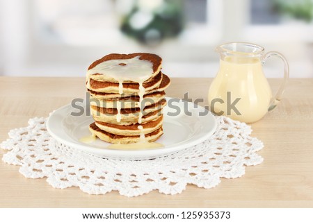 Sweet pancakes on plate with condensed milk on table in kitchen