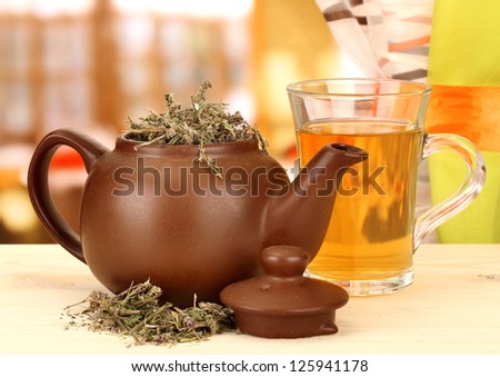 Dried herbs in teapot on wooden table, on bright background. Conceptual photo of herbal tea.
