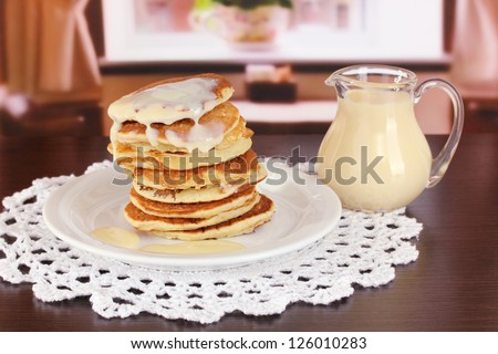 Sweet pancakes on plate with condensed milk on table in room