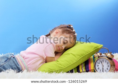 cute little girl sleeping on colorful pillows, on blue background
