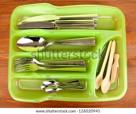 Green plastic cutlery tray with checked cutlery and wooden spoons on wooden table