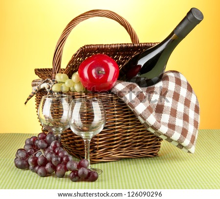 Picnic basket and bottle of wine on cloth on yellow background