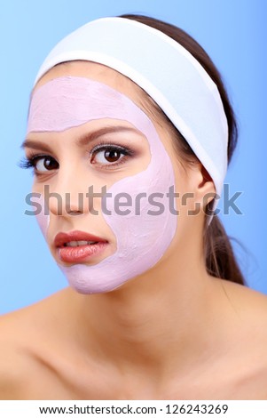 Young woman with clay facial mask on blue background Young woman with clay facial mask on blue background