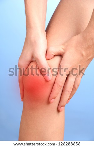 woman holding sore knee, on blue background