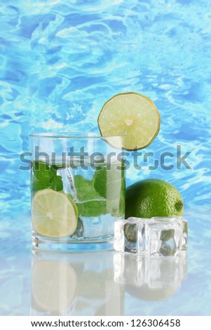 Glass of water with ice, mint and lime on sea background