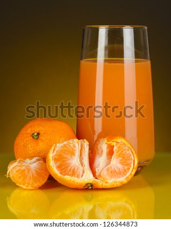 Delicious tangerine juice in glass and mandarins next to it on dark orange background