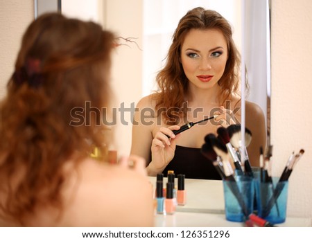 Young beautiful woman making make-up near mirror