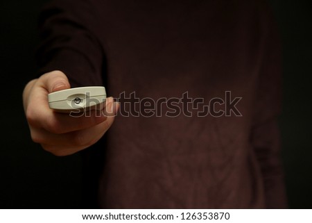 Woman hand holding a TV remote control, on dark background