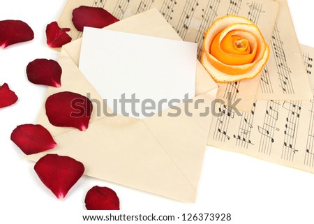 Old envelope with blank paper and dried rose petals on music sheets close up