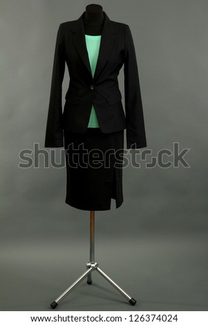 Turquoise blouse and black skirt with coat on mannequin on grey background