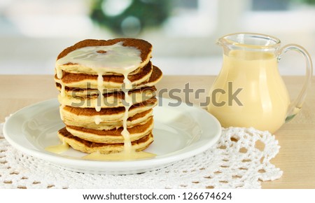 Sweet pancakes on plate with condensed milk on table in kitchen