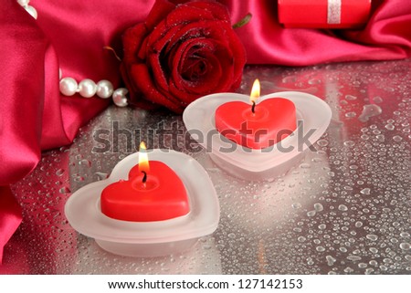 Beautiful candles, rose and red silk on grey wet background