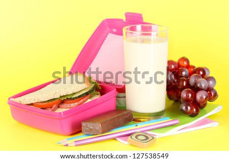 Lunch box with sandwich,grape,milk and stationery on yellow background