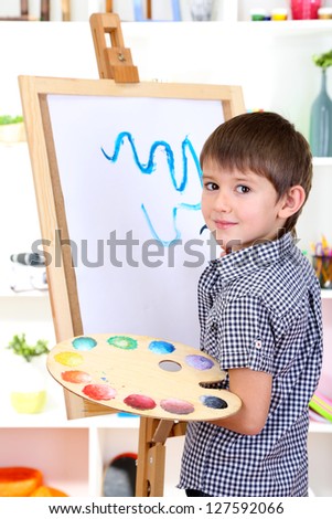 Little boy painting paints picture on easel
