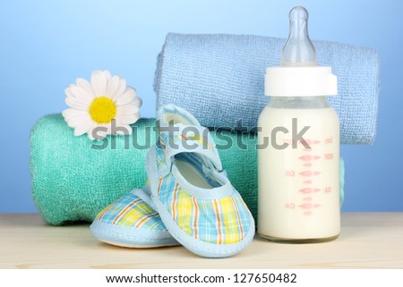 Baby bottle of milk with baby's bootees near towels on blue background
