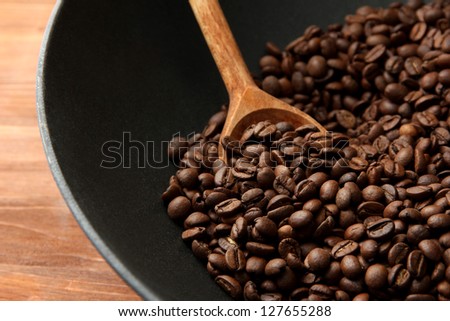 Black wok pan with coffee beans on wooden table, close up
