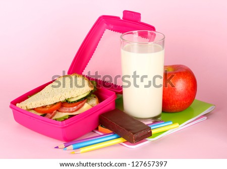 Lunch box with sandwich,apple,milk and stationery on pink background