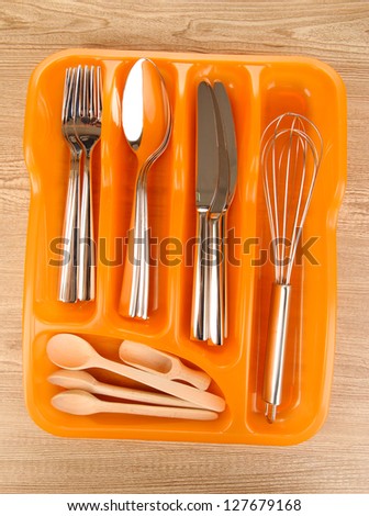 Orange plastic cutlery tray with checked cutlery and wooden spoons on wooden table