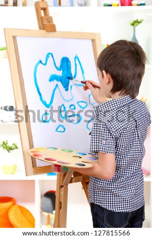 Little boy painting paints picture on easel
