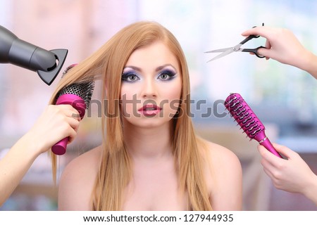 Beautiful woman and hands with brushes, scissors and hairdryer in beauty salon