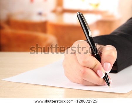 Hand with pen on white paper, on wooden  table on  bright background