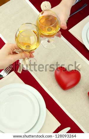 hands of romantic couple toasting their wine glasses over a restaurant table
