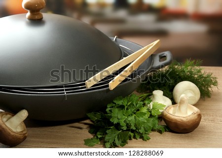 Black wok pan and mushrooms  on kitchen wooden table, close up