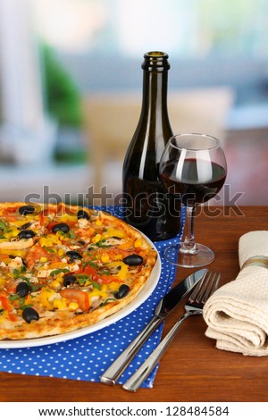 Tasty pizza with wine on wooden table on room background close-up