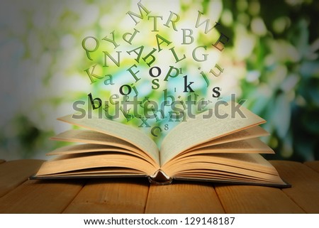 Opened book with letters flying out of it on bright background