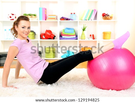 Young woman doing fitness exercises with gym ball at home