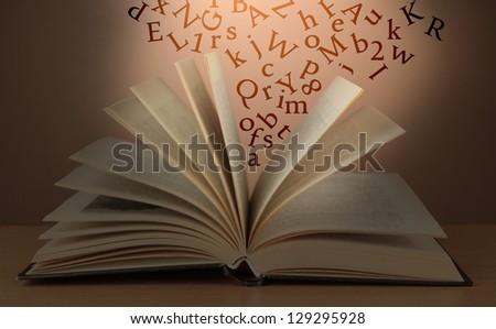 Opened book with letters flying out of it   on brown background