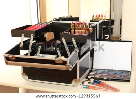 Open case with cosmetics on table near mirror
