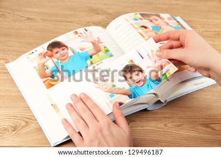 Photos in hands and photo album on wooden table