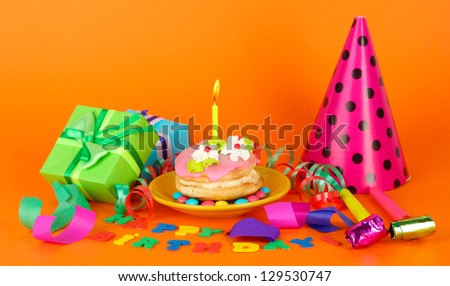 Colorful birthday cake with candle and gifts on orange background