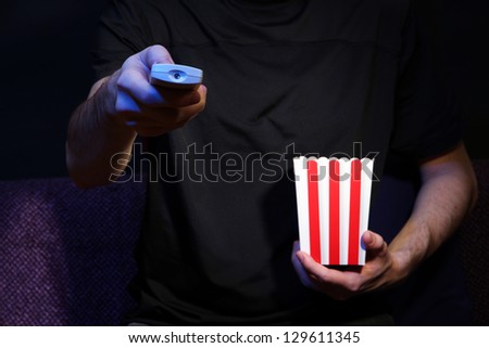 Man hand holding a TV remote control and popcorn, on dark background