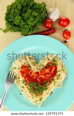 Cooked spaghetti carefully arranged in  heart shape and topped with tomato sauce, on  wooden background