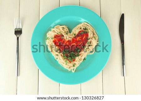 Cooked spaghetti carefully arranged in  heart shape and topped with tomato sauce, on wooden background