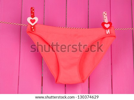 Womans panties hanging on a clothesline, on pink wooden background