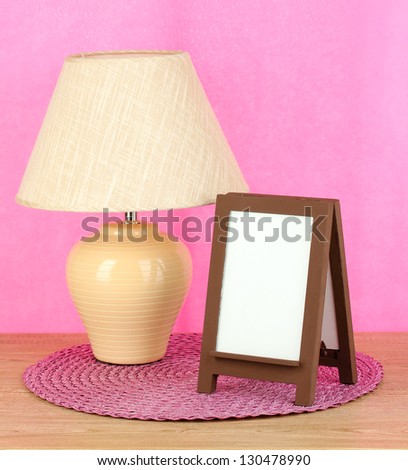 Brown photo frame and lamp on wooden table on pink wall background