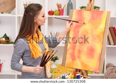 beautiful young woman painter at work, on room interior background