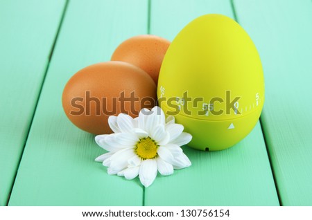 Green egg timer and eggs, on color  wooden background