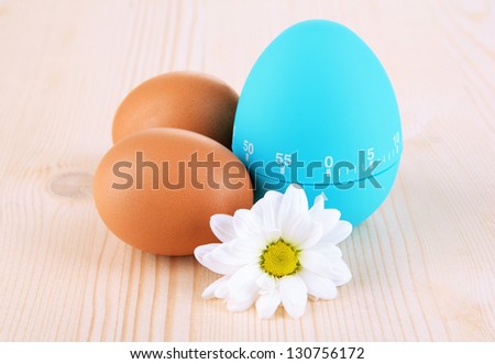 Blue egg timer and eggs, on wooden background