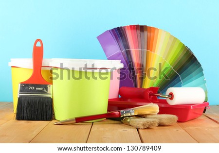 Paint pots, paintbrushes and coloured swatches on wooden table on blue background