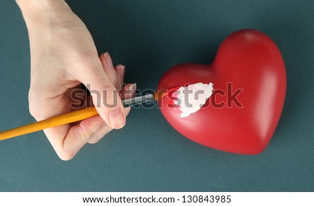 Hand paints white spot on heart, on color background. Conceptual photo treatment of heart disease.