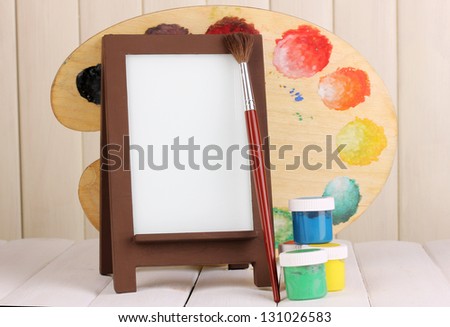 Photo frame as easel with artist\'s tools on wooden background