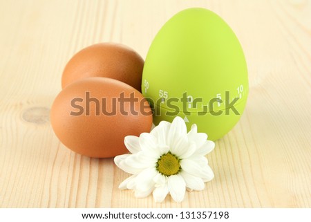 Green egg timer and eggs, on wooden background